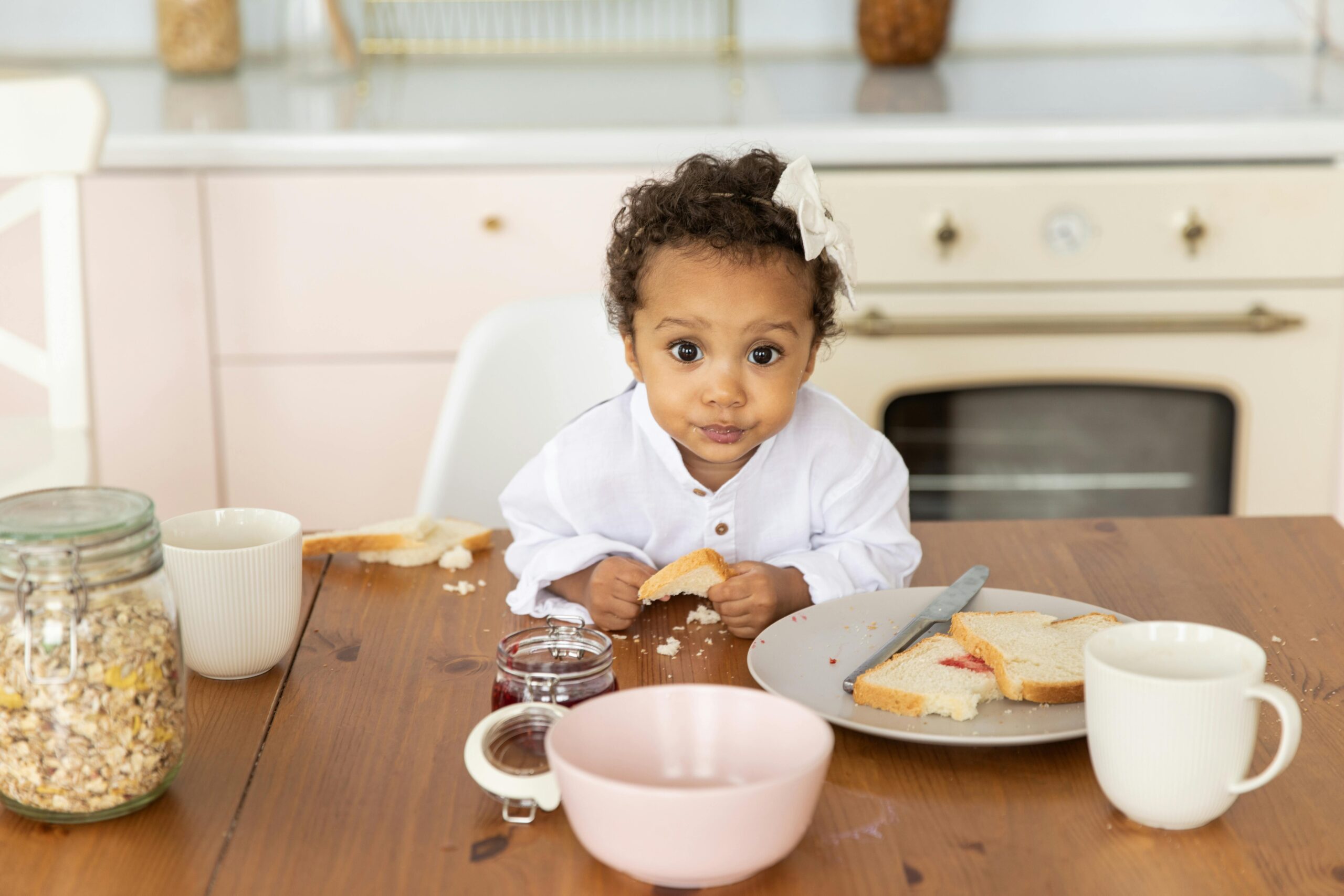 A Little Girl Eating Bread over the Dining Table